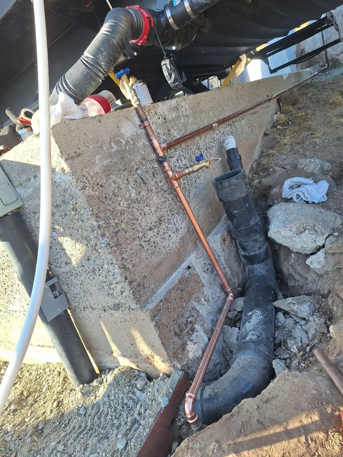 Exposed copper water line and black drainage pipe along foundation