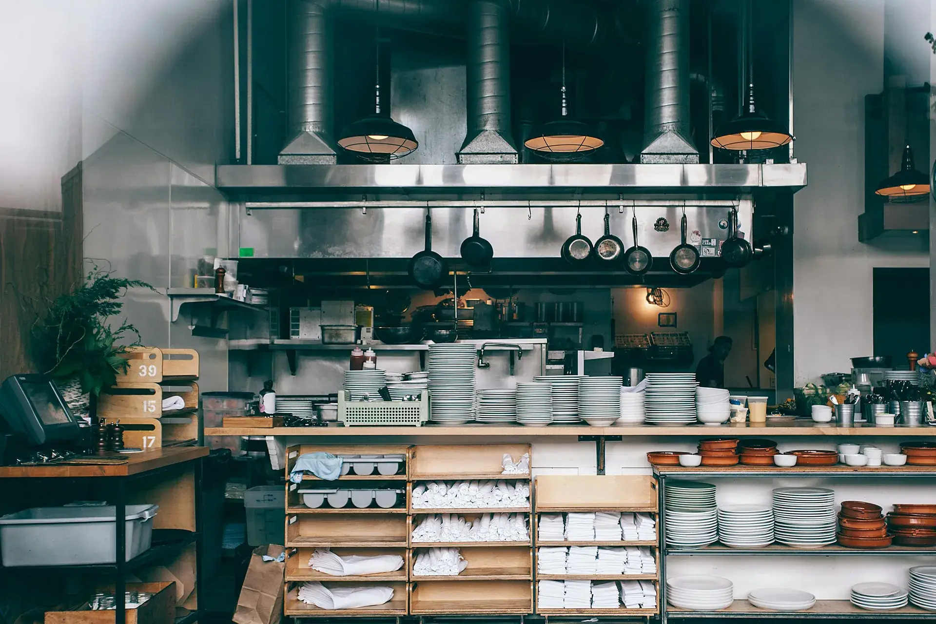 Clean commercial kitchen with neatly stacked plates and visible ventilation above cooking area